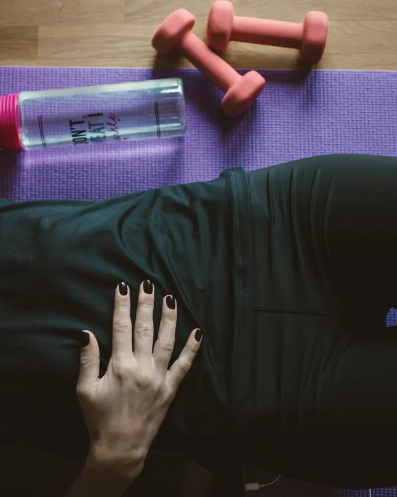 A hand resting on a hip on an exercise mat beside light dumbbells